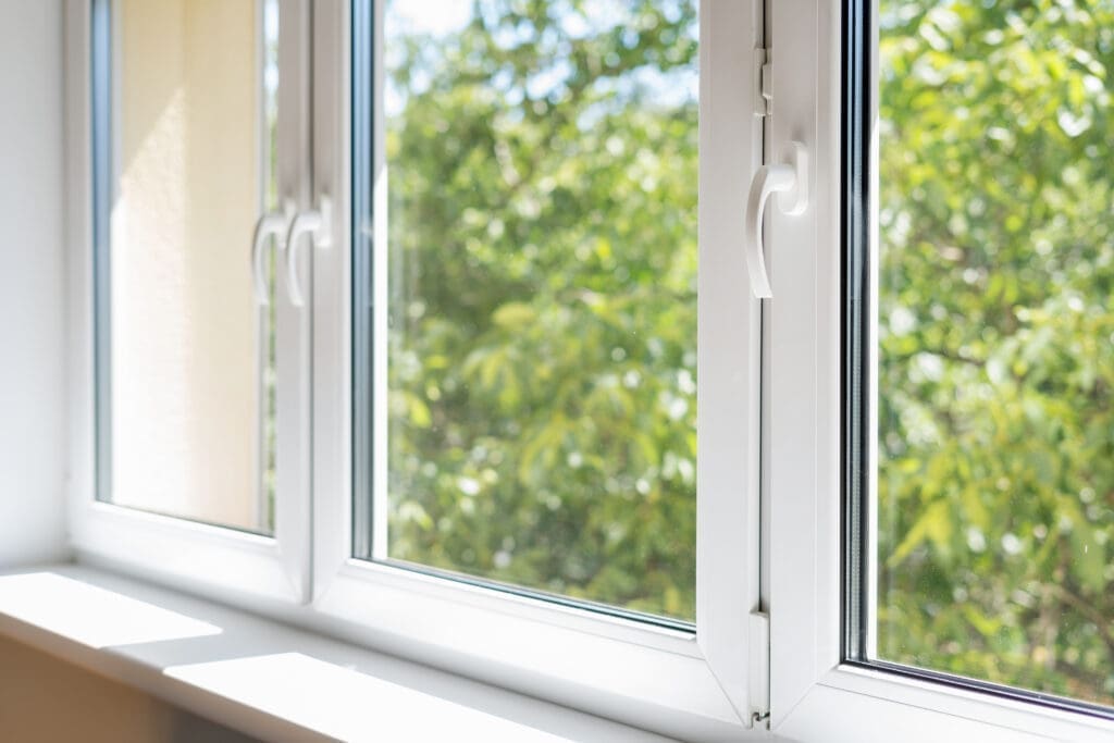 A few residential windows with white frames that are closed and show green trees and a blue sky outside