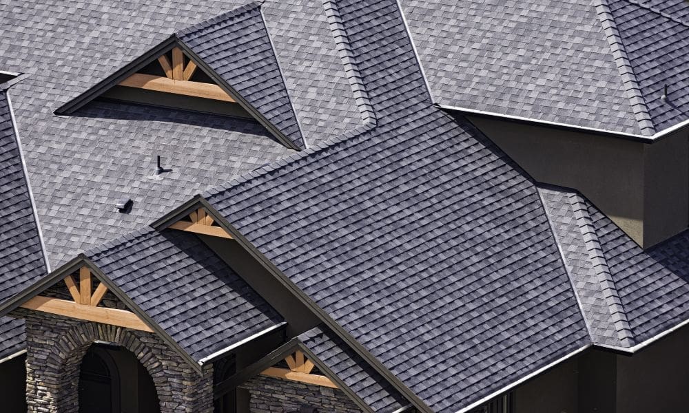 A brand new multicolored gray asphalt shingle roof adorns a newly built home with a dark gray brick front.