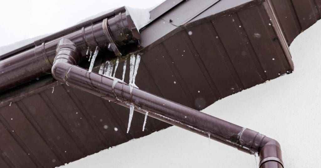 An ice dam has begun to form on a home in the winter. The soffit and gutters are dark brown and full of ice.