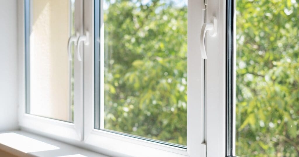 The closed windows of a home show greenery outside. Each window is rectangular with white borders and thin handles.