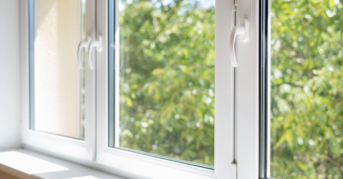 The closed windows of a home show greenery outside. Each window is rectangular with white borders and thin handles.