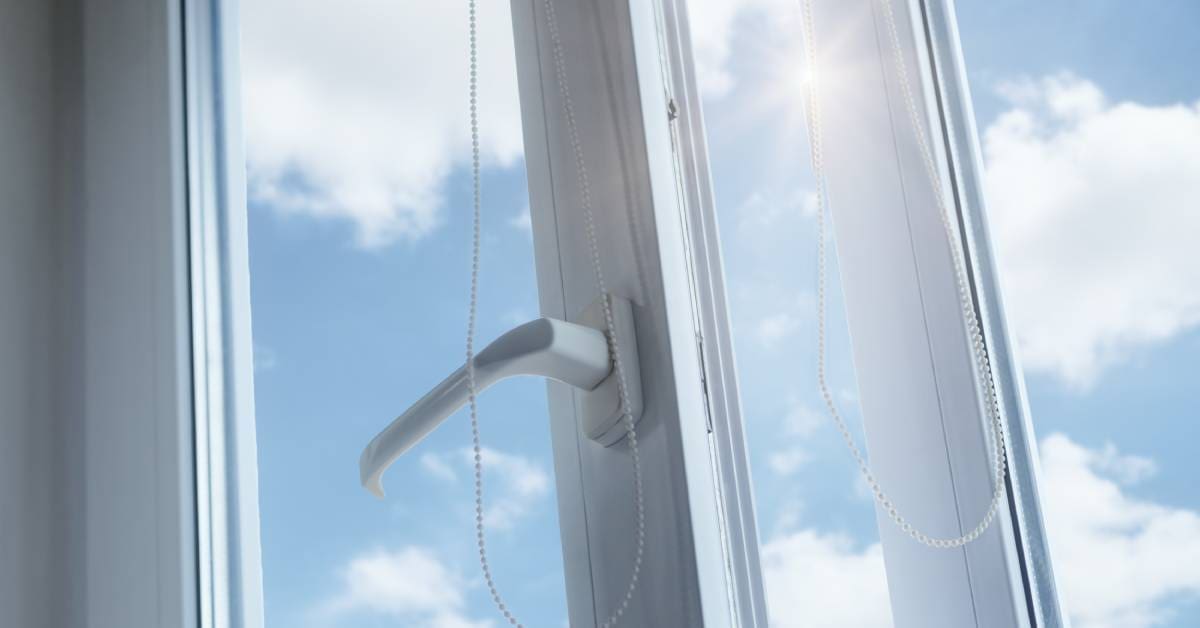 A plastic-bordered window remains ajar as fresh air and sunlight enter a room. A partly cloudy sky is visible outside.