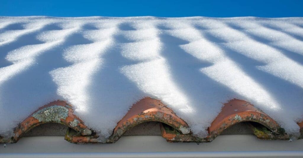 A tiled roof with a thick covering of snow. The visible tiles show signs of mold growth and deterioration.