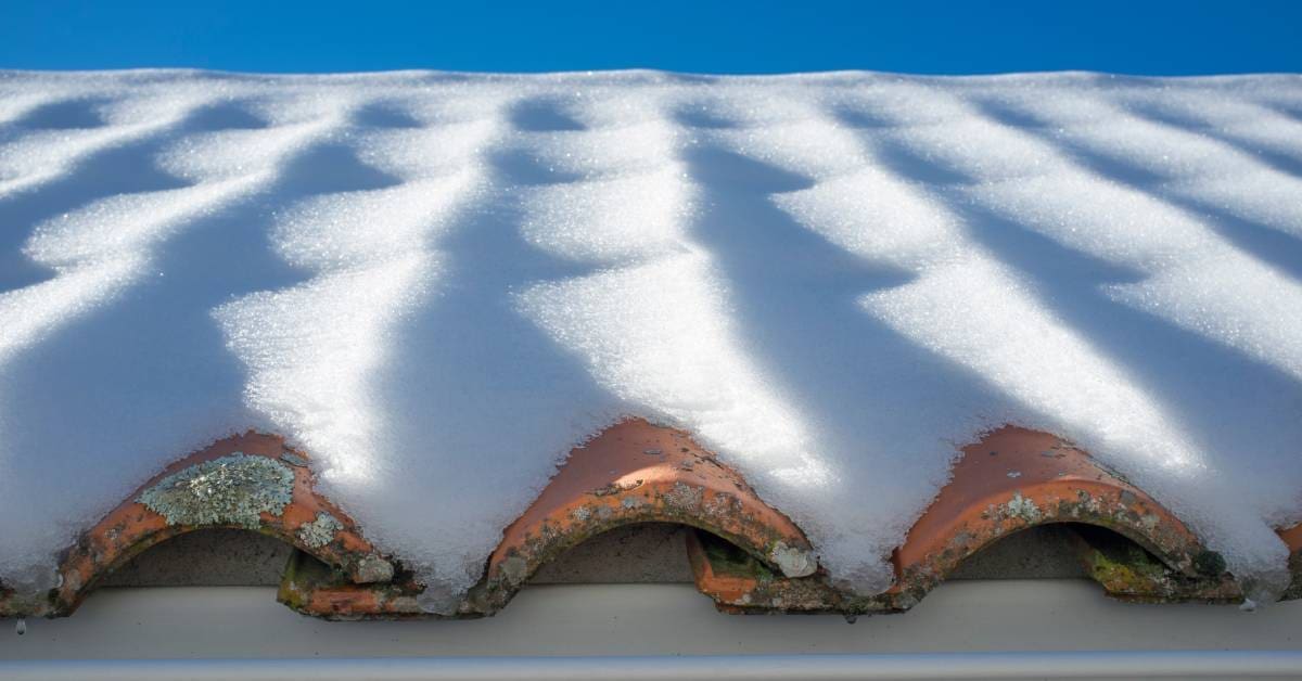 A tiled roof with a thick covering of snow. The visible tiles show signs of mold growth and deterioration.