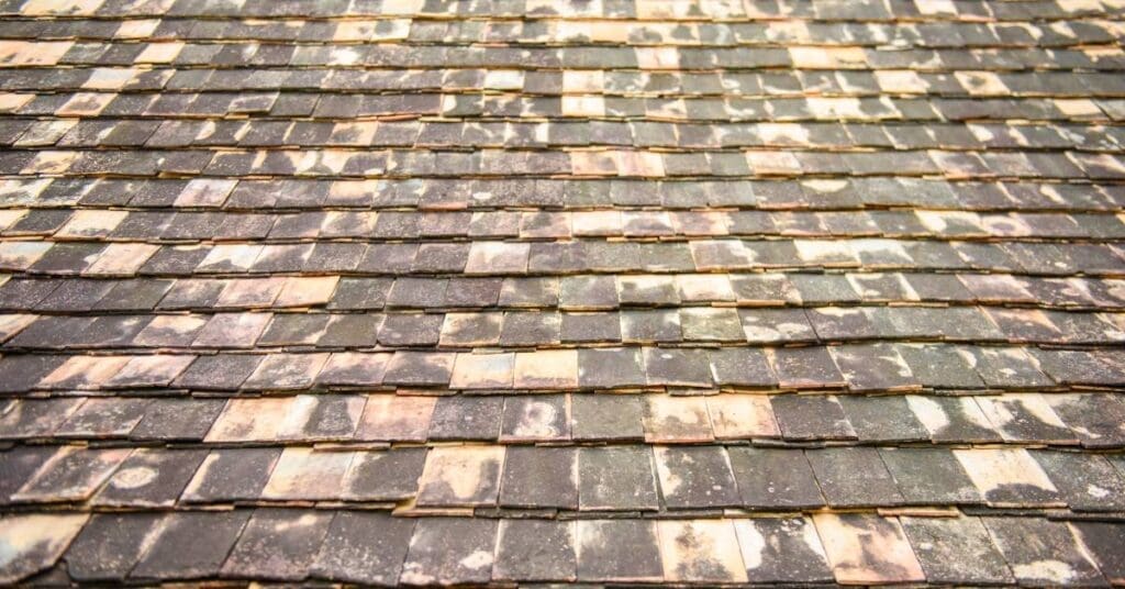 A roof with scattered black asphalt shingles showing signs of discoloration as they turn to a pale orange color.