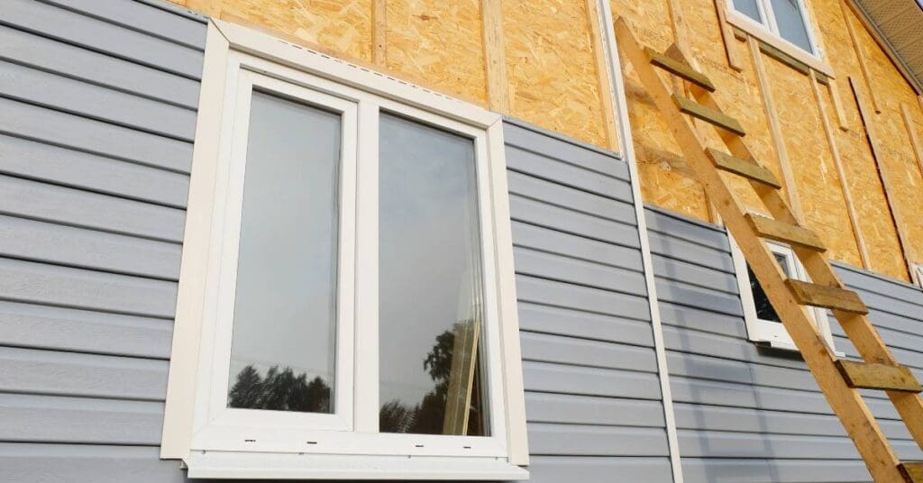 A home under construction with the top half of one side revealing plywood while the other half has installed vinyl siding.