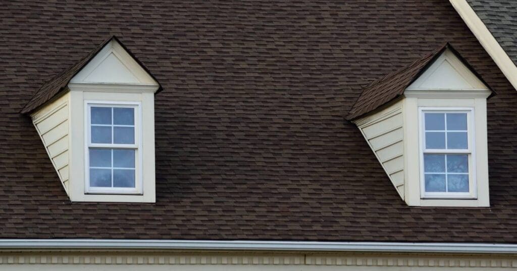 A brick hose with dark brown roof shingles. Two dormers protrude from the roof with white siding and opaque windows.