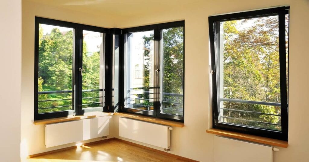 The corner of a room with large windows allowing light to enter. One window tilts forward to open and allow air inside.