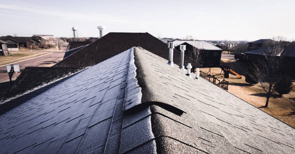 An asphalt roof with one side facing the sun and the other cast in shadow and covered in a layer of frost.