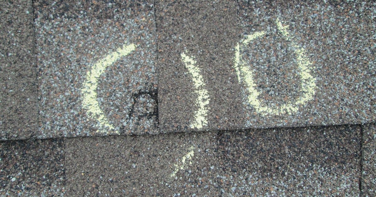 A roof with signs of hail damage in its dented asphalt shingles. Two partial circles mark the location of the damage.