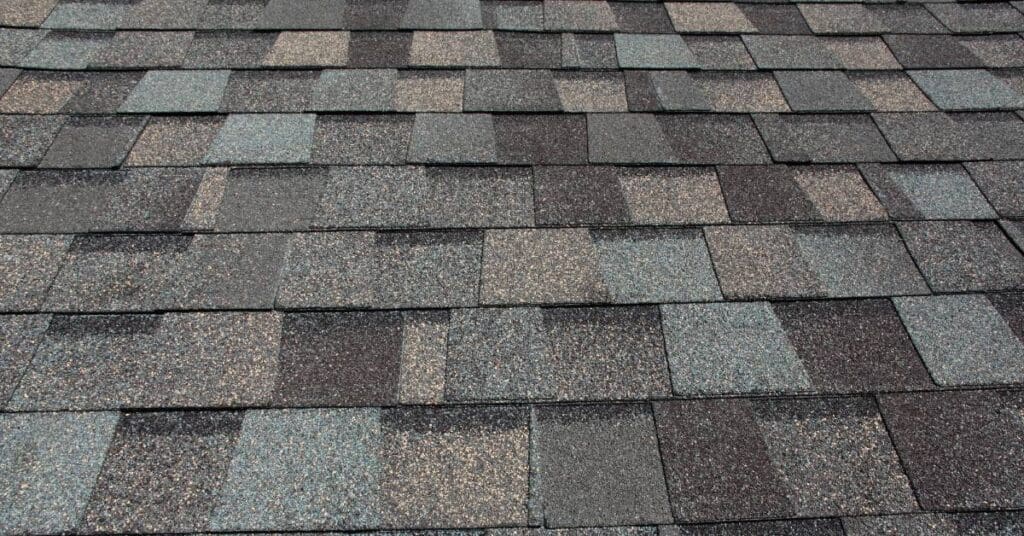 Asphalt shingles of numerous shades of brown have a textured design. They lie in organized rows on a roof.