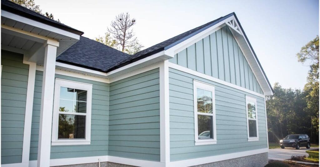 A one-story house with white framing, blue-green siding, black asphalt roof shingles, and a stone foundation.