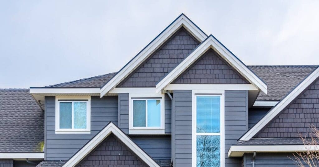 A house with gray-blue siding and black asphalt shingles. Multiple windows with a blue tint are installed on multiple levels.