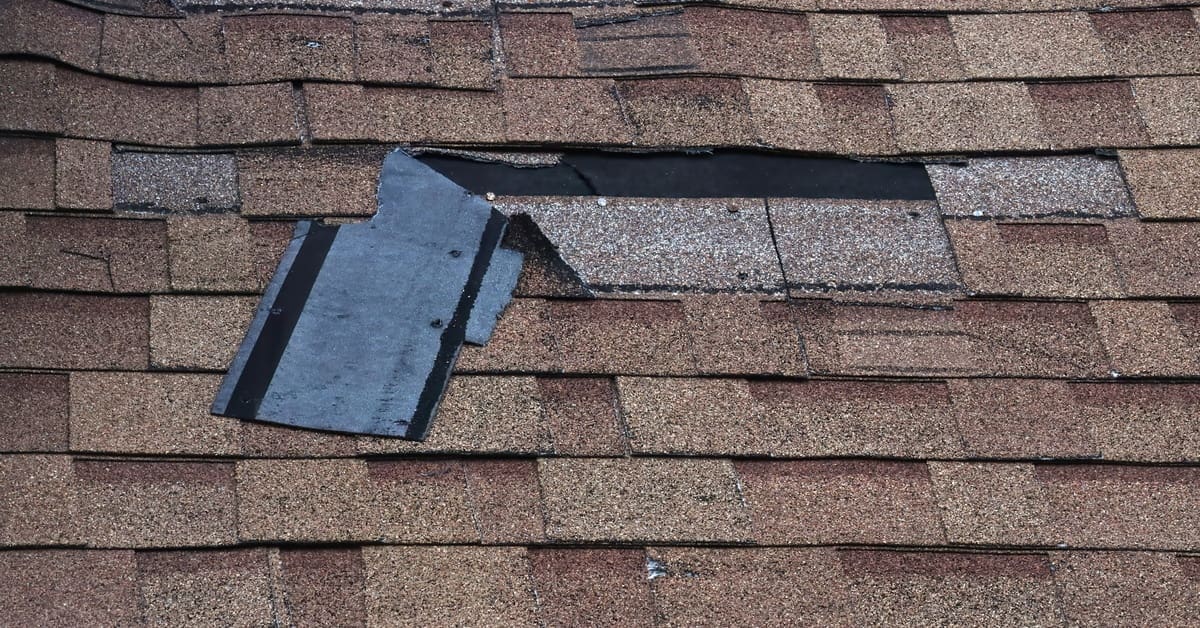 A roof with brown asphalt shingles. Multiple areas of the roof have shingles peeling off to reveal shingles underneath.