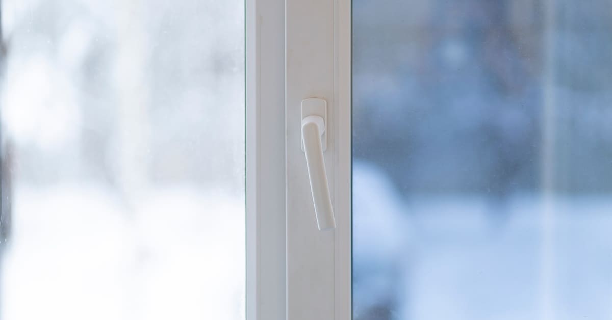 A window with visible tinting features a handle, and the outdoor view beyond the glass appears blurred.