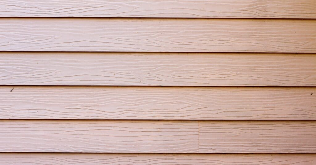 A close-up shows horizontally placed fiber cement siding with a natural wood color and a textured grain finish.