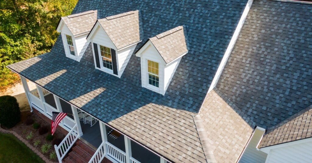 A house with gray asphalt shingles and white siding features a patio with white railings and a US flag.