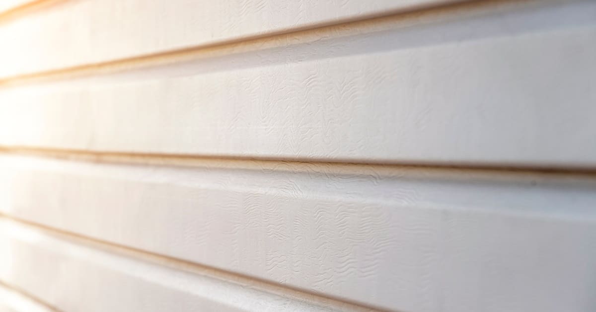 Natural light reflects off beige vinyl siding, revealing its visible texture and horizontal panel lines.