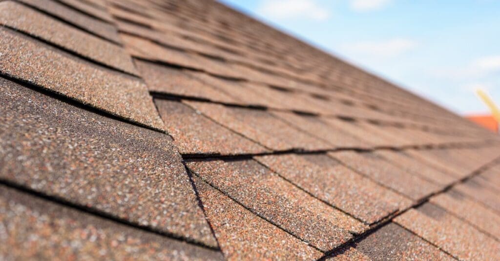 The granules on reddish brown asphalt shingles reflect flecks of red, orange, and white in the sunlight.