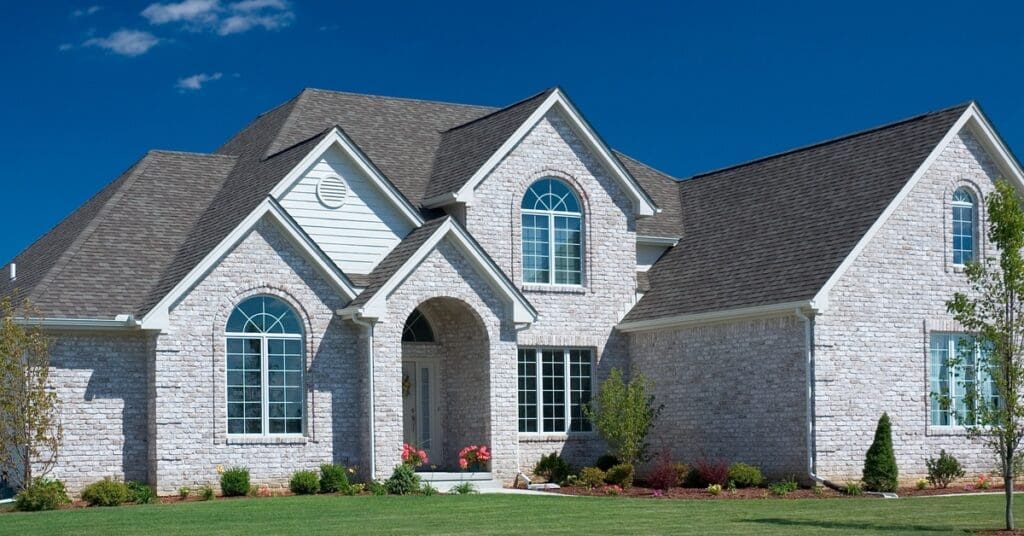 A front-side view of a beautiful, white home with a well-maintained, black roof. The home has landscaping in the front yard.