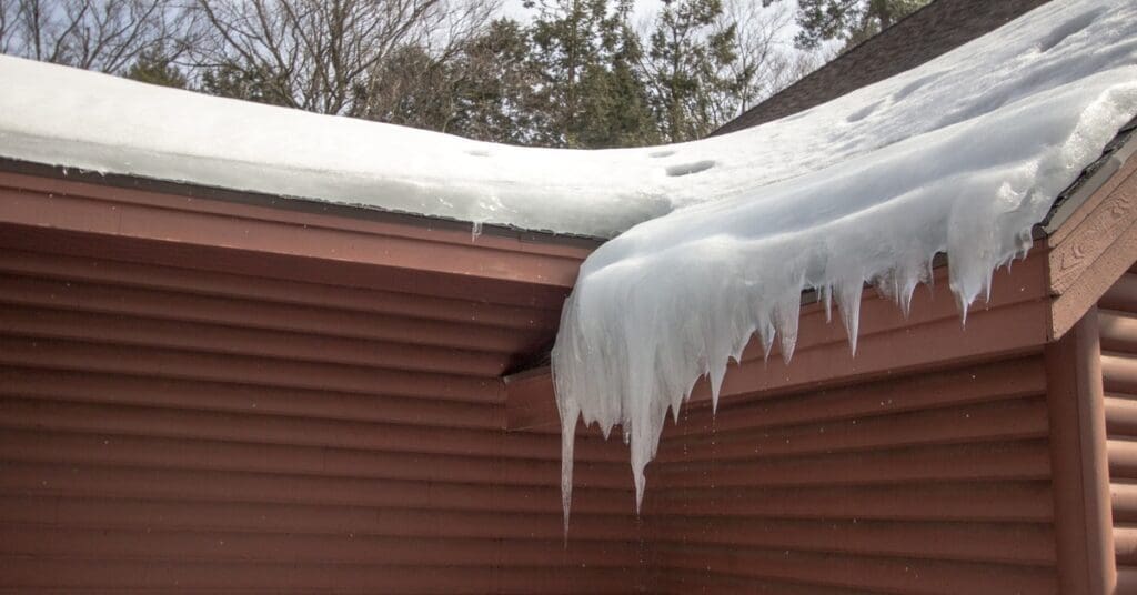 The corner of a cabin roof in the winter. An accumulation of ice and snow is on the lower end of the roof, forming an ice dam.