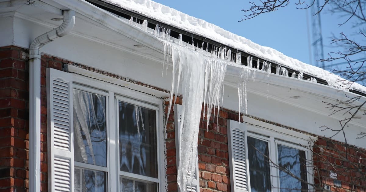 A close-up of a red brick home's roof in the winter. A very large ice dam is heavily weighing down the gutter.