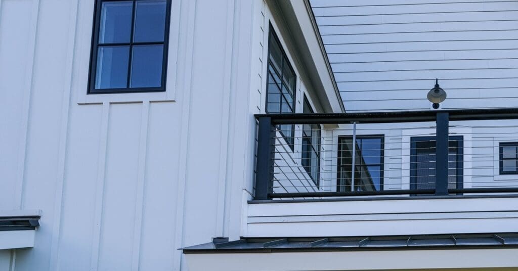 A modern home contains white fiber cement siding and a balcony with a black railing and a light above the door.