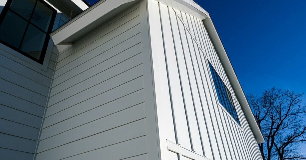 A home contains vertical and horizontal white fiber cement siding. There is a bright blue sky in the background.