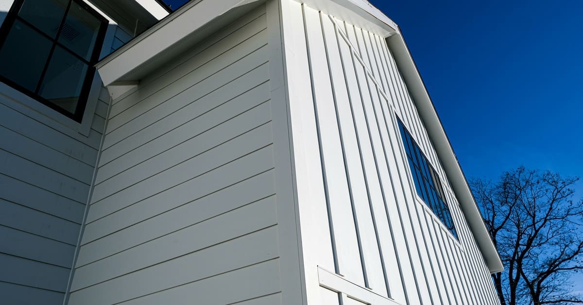 A home contains vertical and horizontal white fiber cement siding. There is a bright blue sky in the background.