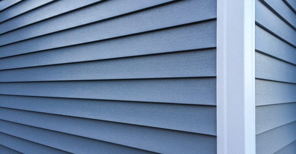 Blue lap siding extends across a home's exterior wall, meeting a crisp white corner trim board at a right angle.
