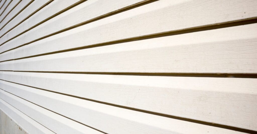 White lap siding panels stretch horizontally across a house exterior, displaying wood grain texture and deep shadow lines.