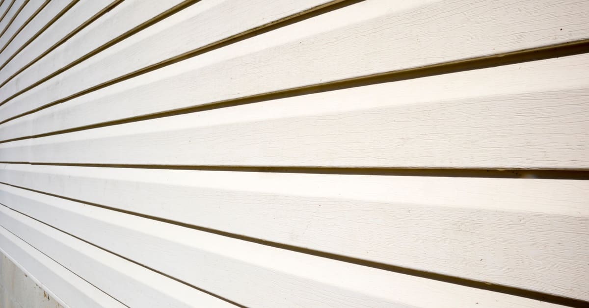 White lap siding panels stretch horizontally across a house exterior, displaying wood grain texture and deep shadow lines.
